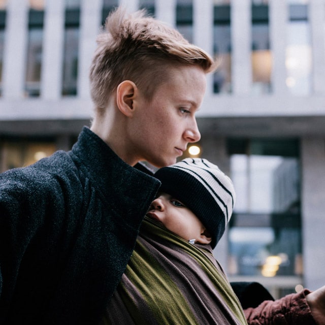 A mother walking with her baby in a wrap carrier through the city